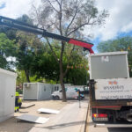 Vista frontal de dos módulos prefabricados tipo camerino instalados por Europa Prefabri para el Ayuntamiento de Pinto, con acceso independiente y acabados en blanco. En el entorno se aprecia una zona urbana destinada a actividades culturales.