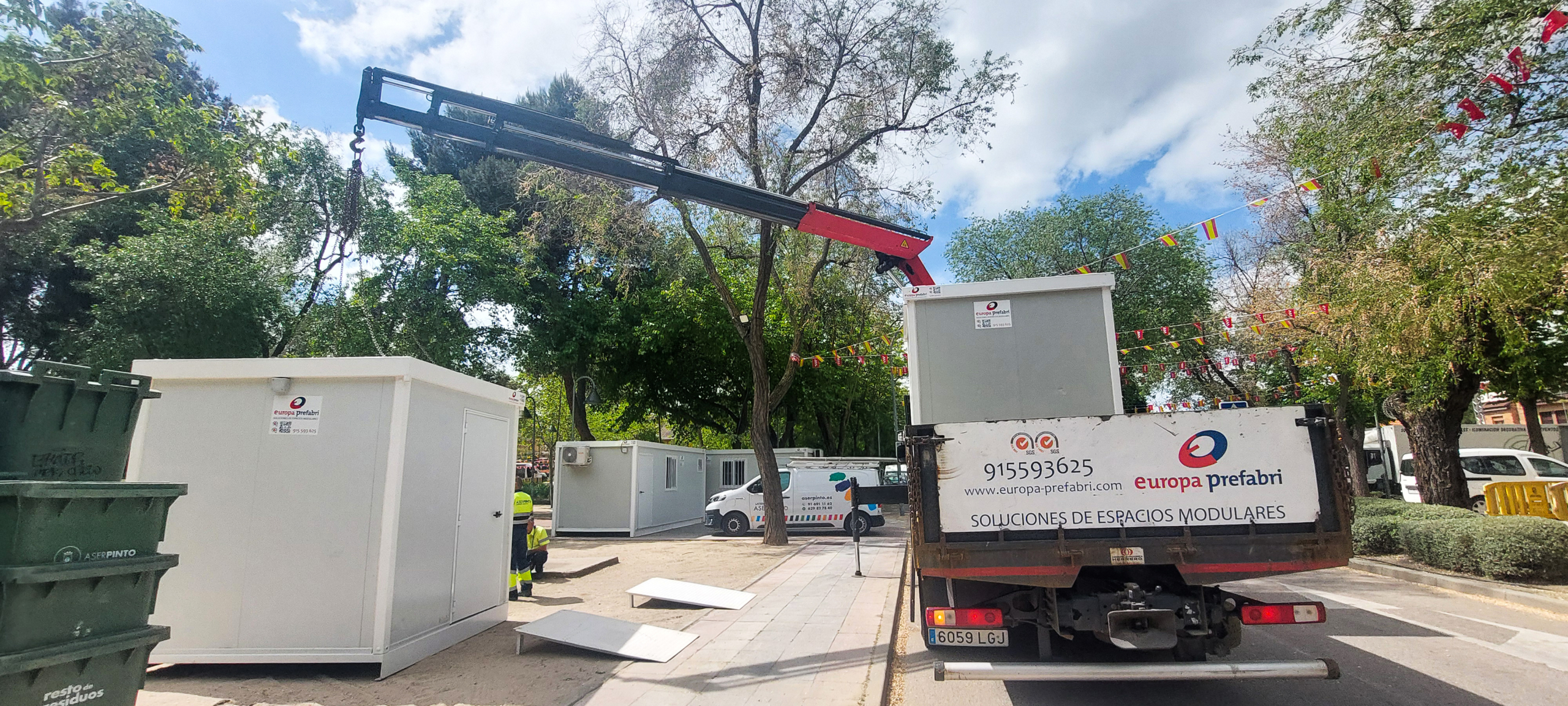 Vista frontal de dos módulos prefabricados tipo camerino instalados por Europa Prefabri para el Ayuntamiento de Pinto, con acceso independiente y acabados en blanco. En el entorno se aprecia una zona urbana destinada a actividades culturales.