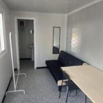 Interior de un módulo camerino equipado, mostrando el mobiliario instalado: sofá, mesa, espejo de cuerpo entero y sillas. El espacio está diseñado para ofrecer comodidad y funcionalidad a los artistas antes de una actuación.